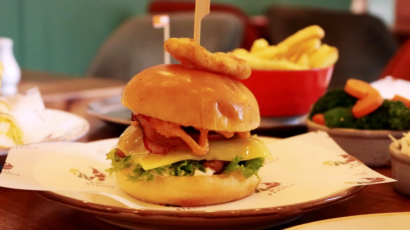 A stacked burger topped with an onion ring, with chips behind